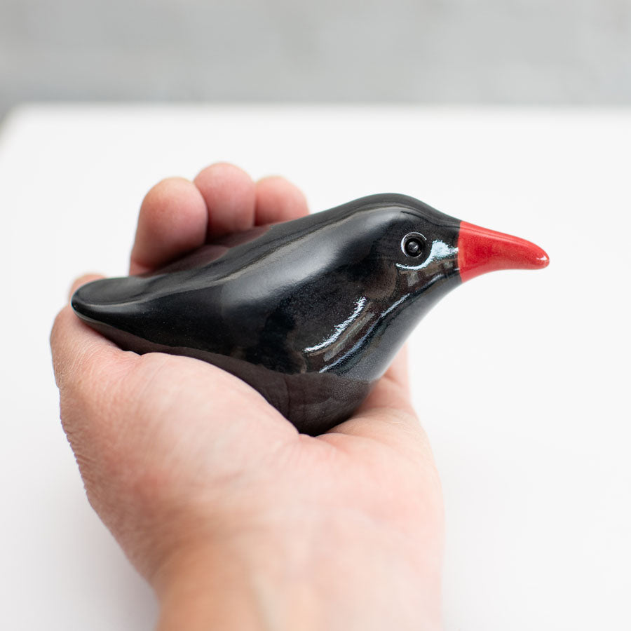 A small ceramic Chough sculpture against a plain background in a hand