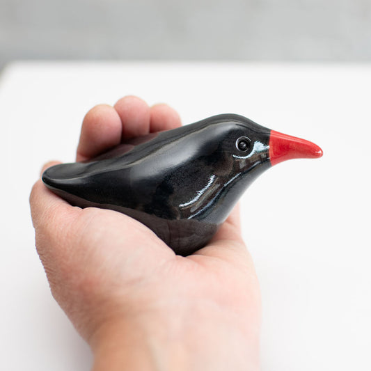 A small ceramic Chough sculpture against a plain background in a hand