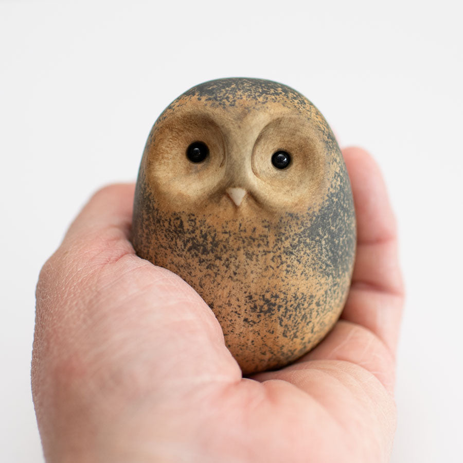 Small ceramic Tawny Owl sculpture in a hand against a white background