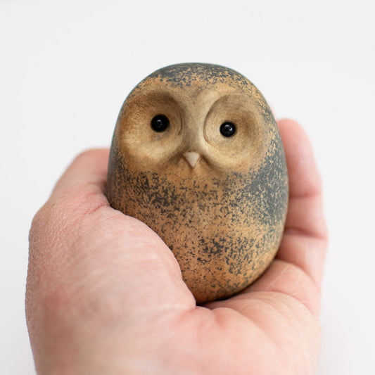 Small ceramic Tawny Owl sculpture in a hand against a white background