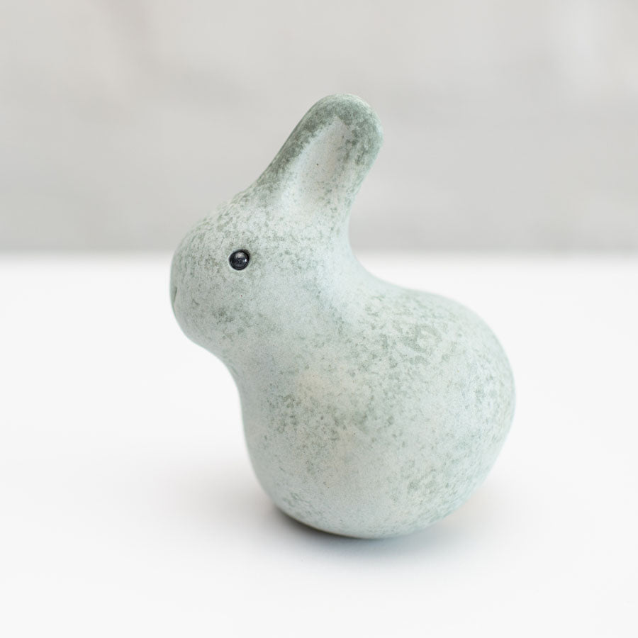 A small grey ceramic bunny sculpture against a grey background