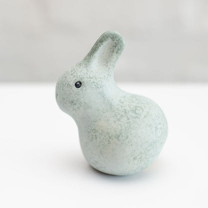 A small grey ceramic bunny sculpture against a grey background