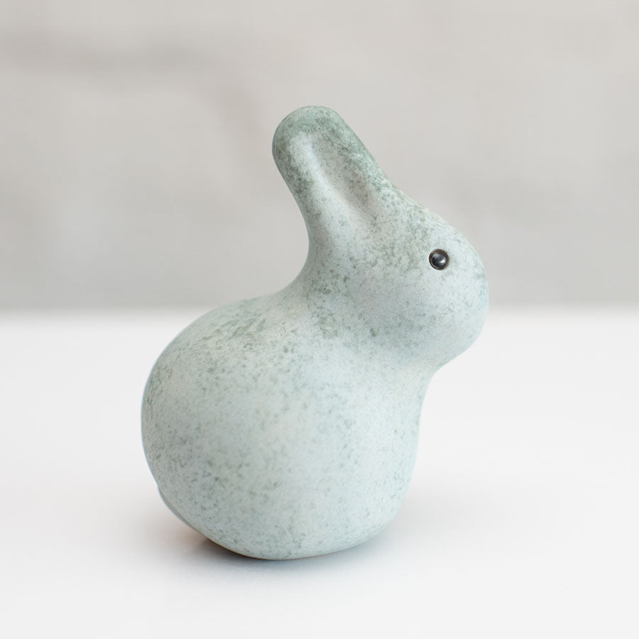 A small grey ceramic bunny sculpture against a grey background