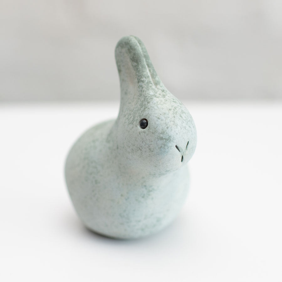 A small grey ceramic bunny sculpture against a grey background