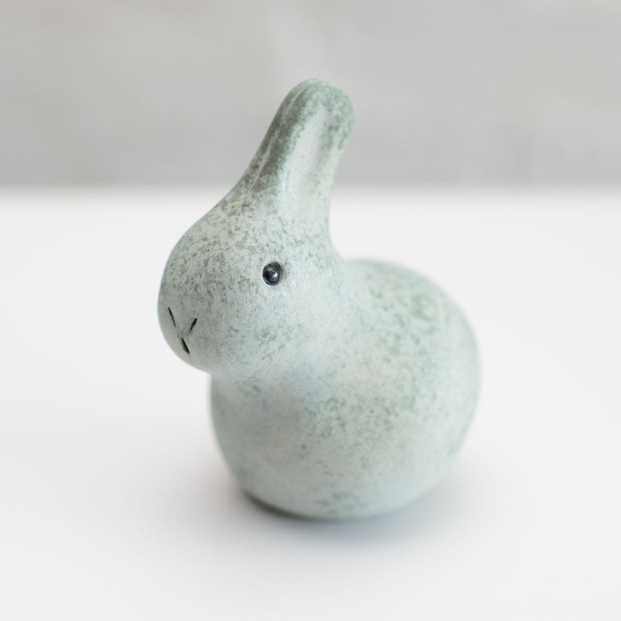 A small grey ceramic bunny sculpture against a grey background