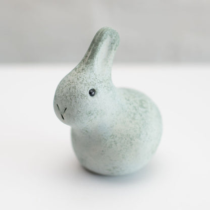 A small grey ceramic bunny sculpture against a grey background