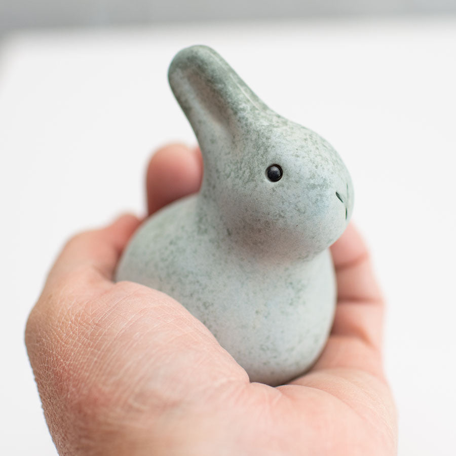 A small grey ceramic bunny sculpture in a hand