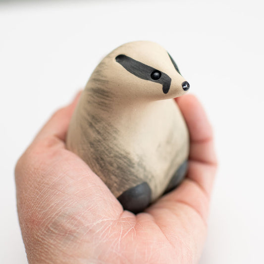 A small badger sculpture sat in a hand against a white background