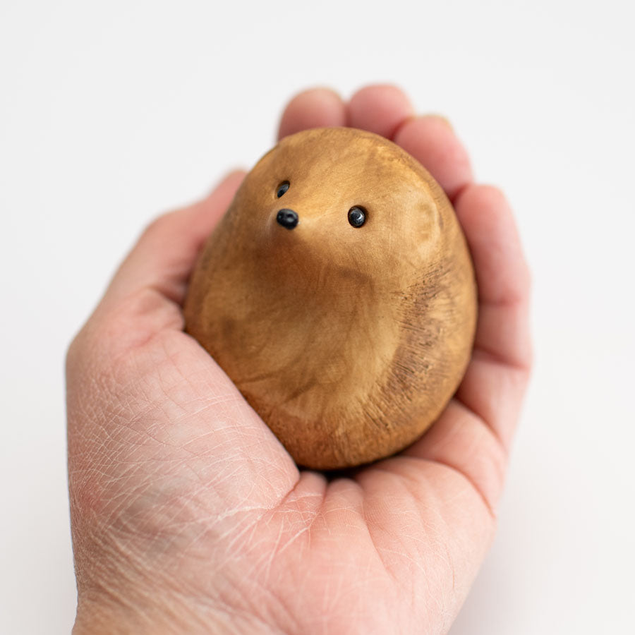 A small brown ceramic hedgehog sculpture in a hand