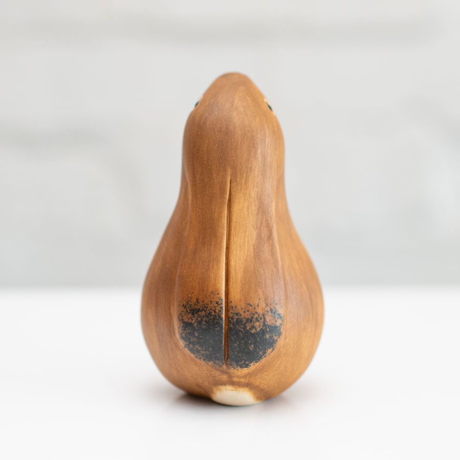 A small ceramic hare sculpture in a chestnut brown colour standing on a white surface against a soft gray background.
