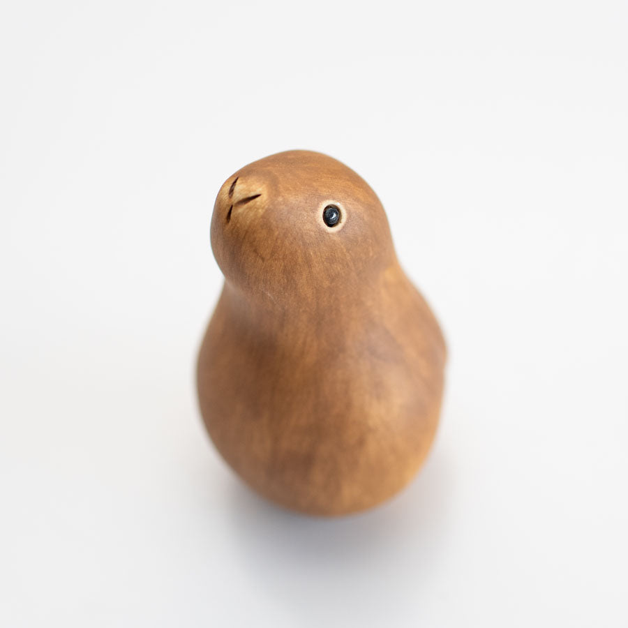 A small ceramic hare sculpture in a chestnut brown colour standing on a white surface against a soft gray background.