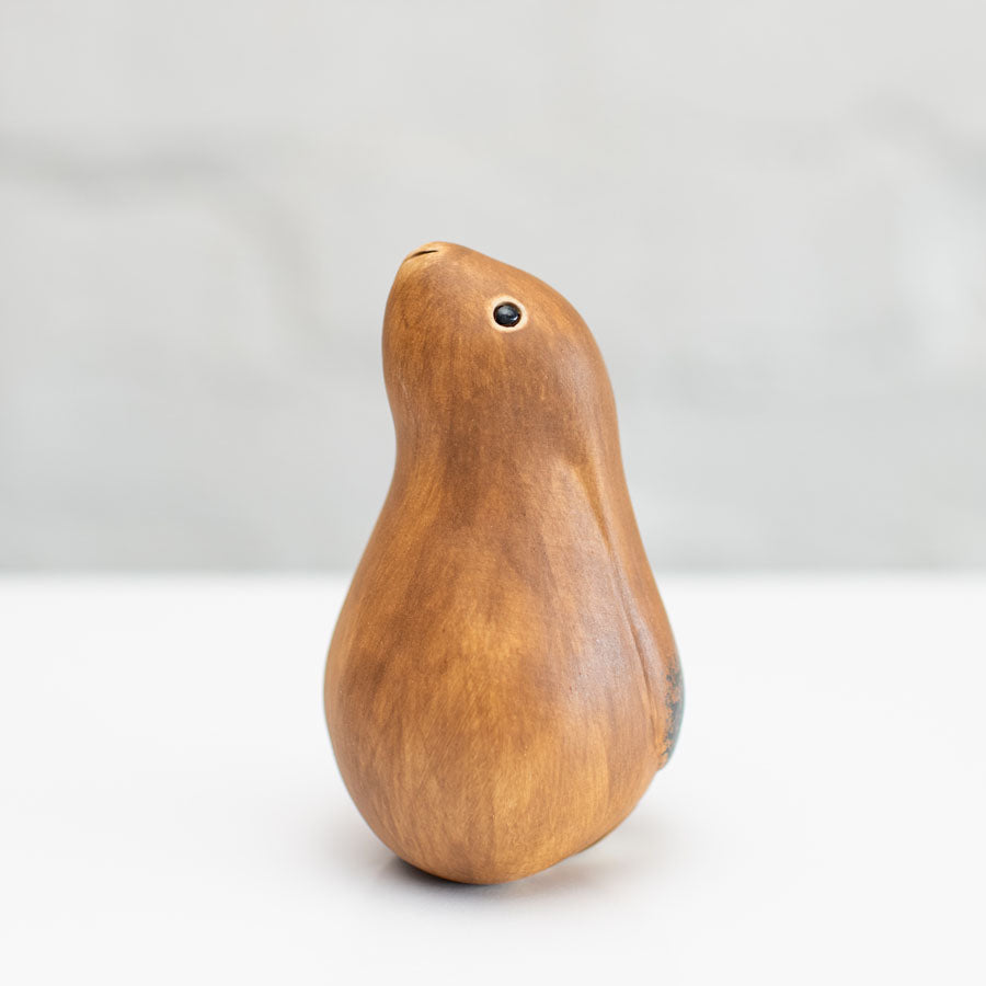 A small ceramic hare sculpture in a chestnut brown colour standing on a white surface against a soft gray background.