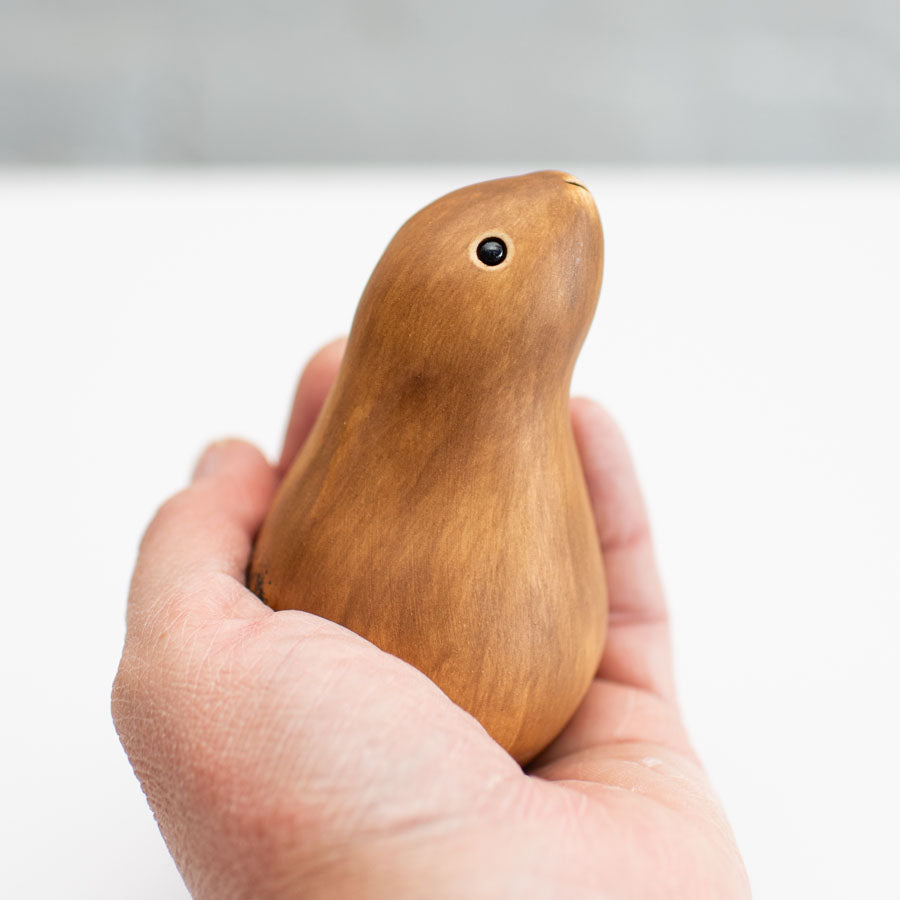 A small ceramic hare sculpture in a chestnut brown colour sitting in a hand against a soft gray background.