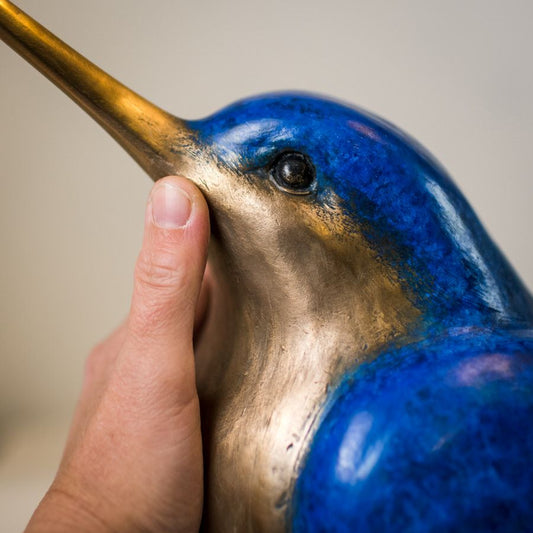 Hand touching the head of a Large Bronze Kingfisher Sculpture, showing its blue and bronze details