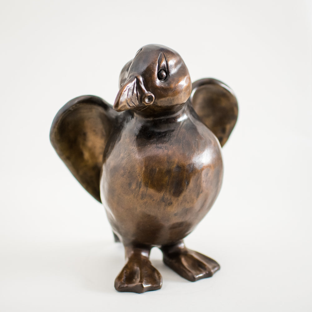A bronze sculpture of a standing Puffin in a traditional brown bronze patina. The surfaces are smooth and he has character