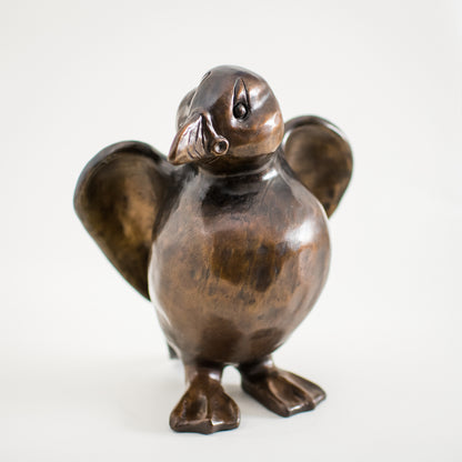 A bronze sculpture of a standing Puffin in a traditional brown bronze patina. The surfaces are smooth and he has character