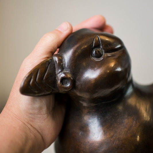 Hand holding a bronze puffin sculpture, showing its head and beak