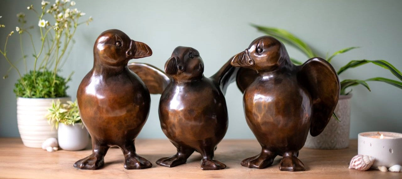 3 bronze puffin sculptures on a wooden surface