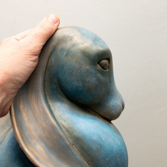 Hand touching the head of a blue and bronze Divine Feminine Power Bronze Hare Sculpture
