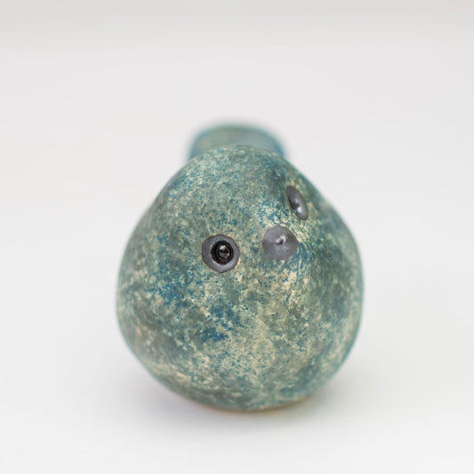 A small ceramic bird in mottled blues and greens with a shiny eye and beak looking at the camera