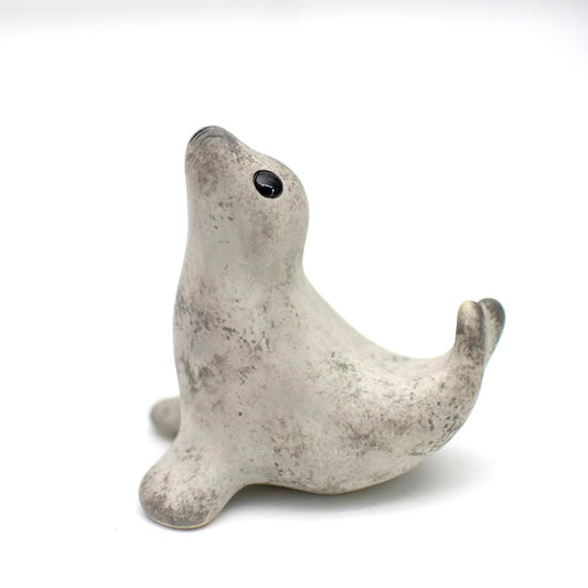 A small ceramic light grey seal in a classic curly pose