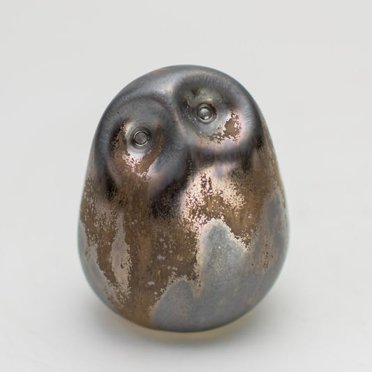 Round smooth small metallic ceramic owl on a plain background