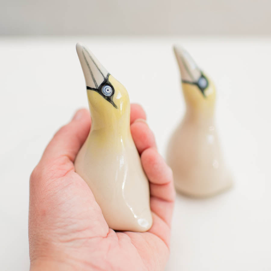 Hand holding a small ceramic gannet sculpture, with another in the background