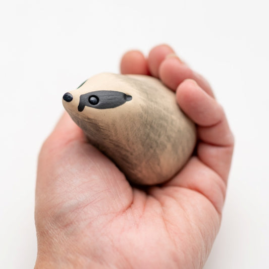 Small ceramic badger sculpture in a hand against a white background