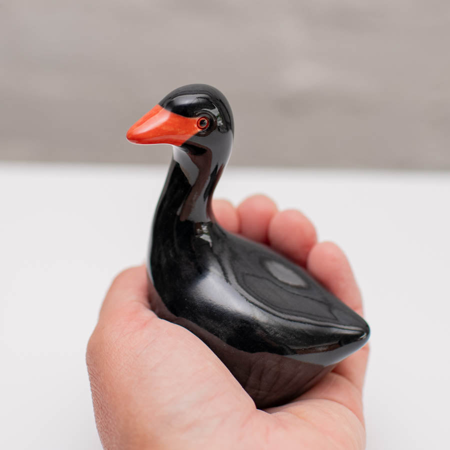 Small ceramic black Swan sculpture in a hand against a white background