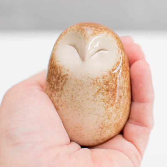 A happy little Barn Owl sculpture against a light background sat in a hand