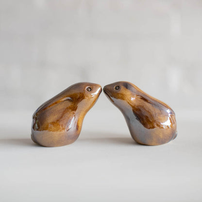 Two small glazed ceramic hares facing each other, on a light gray surface with a soft blurred background.