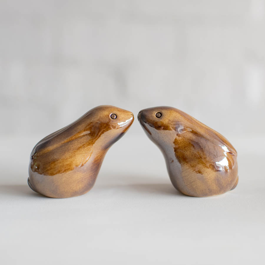 Two small glazed ceramic hares facing each other, on a light gray surface with a soft blurred background.