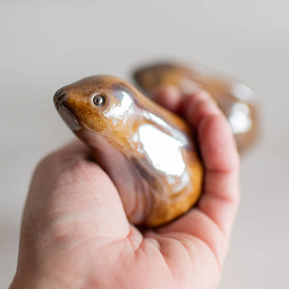 A small glazed ceramic hare figurine in a metallic bronze colour in a hand against a white surface 