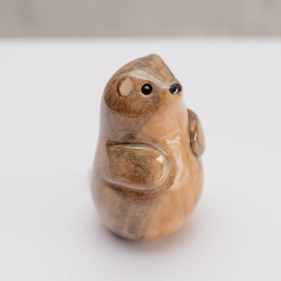 A small glossy ceramic stoat sculpture against a grey backdrop