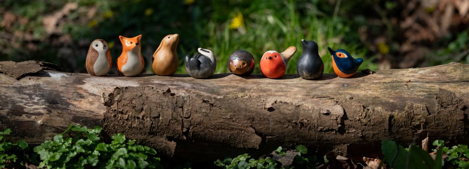 A row of ceramic wildlife sculptures on a log in the woods