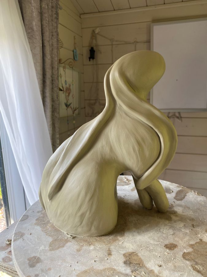 Clay sculpture of a figure with flowing drapery, viewed from the back