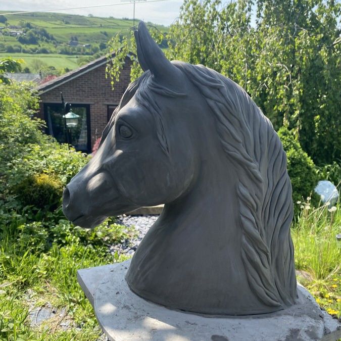 Large horse head sculpture in clay on a stand in a garden