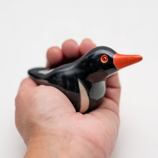 Ceramic Oystercatcher Sculpture held in a hand, black bird with orange beak and eye