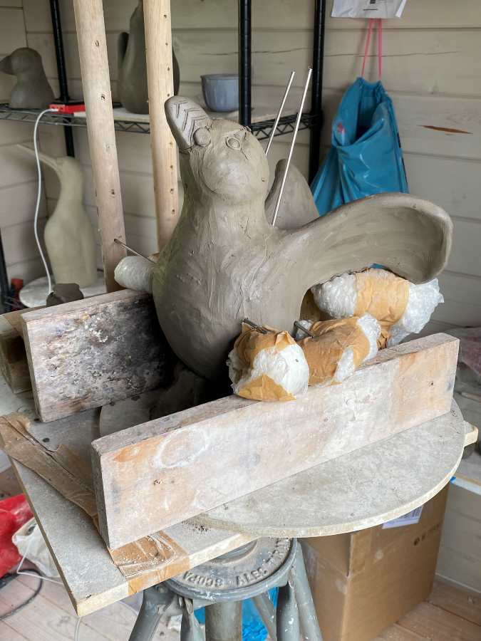 Clay sculpture of a bird with outstretched wings on a wooden stand